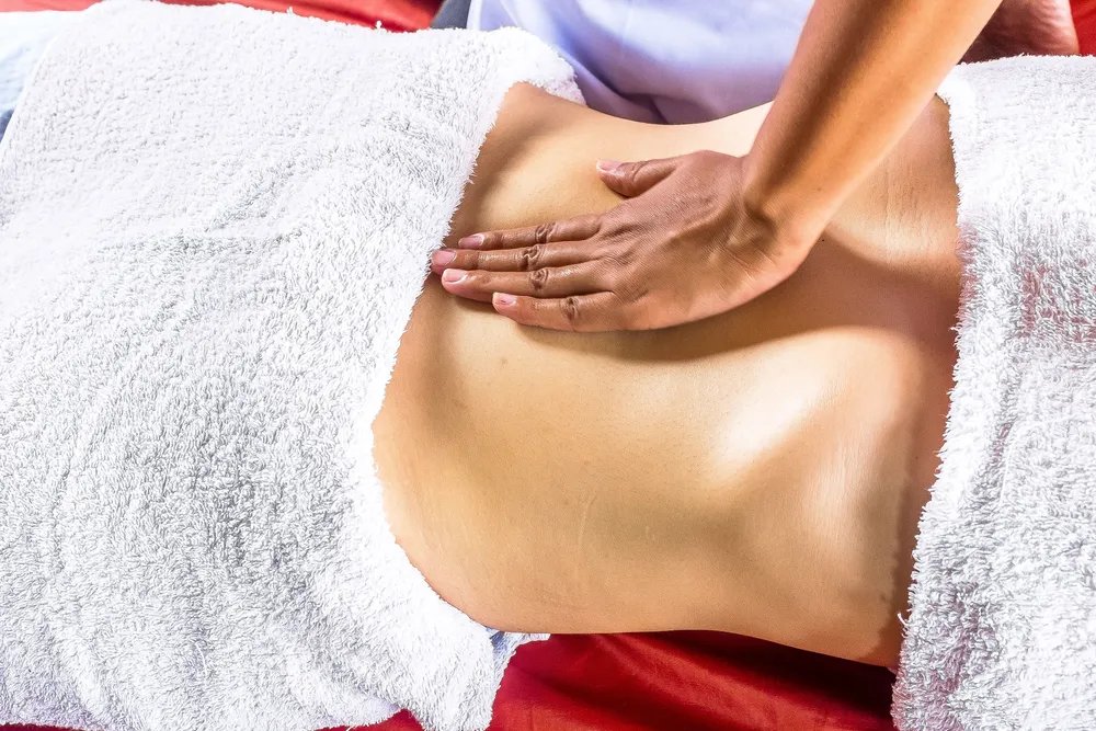 Hände bei der Massage am Rücken einer Klientin auf der Behandlungsliege